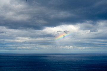 Small colorful rainbow in a stormy ocean sky