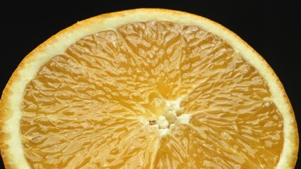 A macrography capture of an orange slice, placed against a sleek, isolated black backdrop, unfolds...