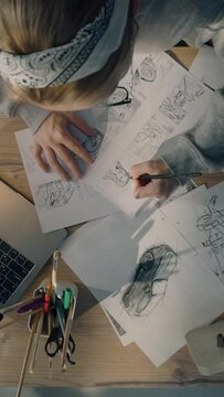 Young female illustrator drawing pencil sketches on paper. Drawings on the sheet of papers in front of her. Illustration animation, storyboard, video game film production, animation design studio.