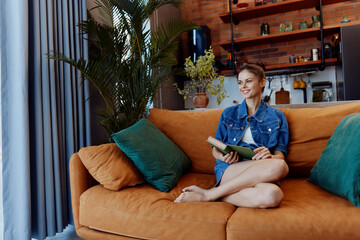 Young woman reading a book on orange couch against rustic brick wall background in cozy home setting