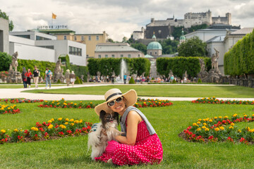 Frau mit Hund sitzt lächelnd im Gras mit gepunktetem Kleid, im Hintergrund die Festung...