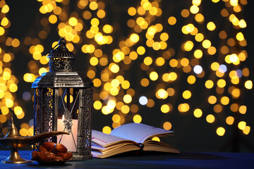 Arabic lantern, Quran, dates and Aladdin magic lamp on table against blurred lights at night. Space...