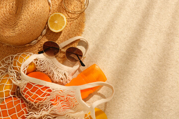 String bag with sunglasses, straw hat and fruits on beige textured background, flat lay. Space for text