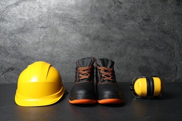 Hard hat, pair of working boots, and earmuffs on gray background, space for text