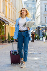 Young blonde woman tourist with luggage suitcase exploring checking paper map search a way direction while traveling abroad. Lady girl walking on urban summer city street. Town lifestyles outdoors