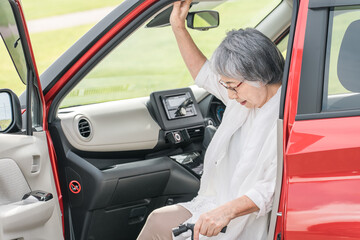 杖をついて車の助手席から降りるシニア・高齢者女性
