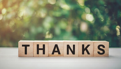 Wooden blocks spell "THANKS" on a white table with a blurred background, symbolizing gratitude, appreciation, and acknowledgment in a simple and heartfelt manner