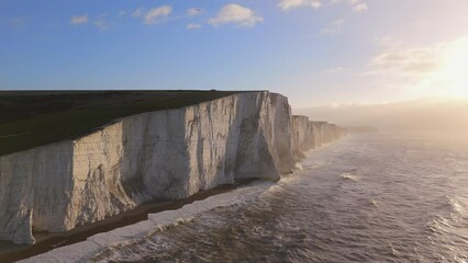 Majestic white cliffs overlook the ocean, with golden light of sunset. Waves crash dramatically below, creating a serene and picturesque landscape that captivates nature enthusiasts. Seven Sisters 