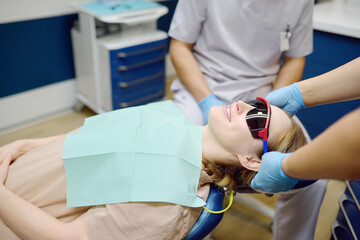 Practitioner dentist doctor prepares woman for teeth treatment in hospital. Assistant wearing protection glasses on patient before orthodontists or prosthetics treatment in modern medical center