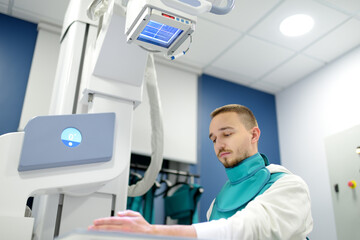 Obraz premium Young man having x-ray shot of broken hand in x-ray room in modern clinic. Patient wearing in protect lead apron