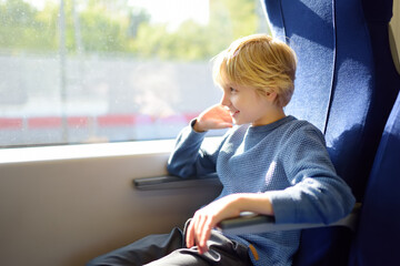 Cute preteen boy is traveling in a local train carriage or by railroad while it rain outside.