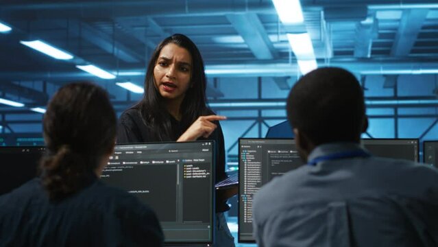 Supervisor in server hub managing multiracial team of programmers looking for equipment misconfigurations. Manager coordinating tech specialists fixing data center damages