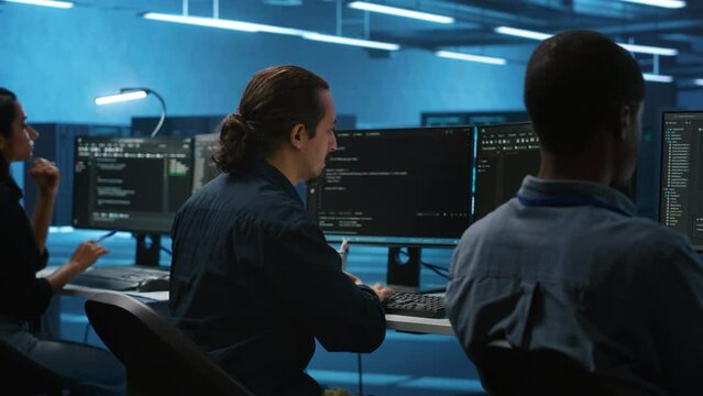 Multiracial coworkers in data center coding and checking parameters on computer. Multiethnic team working together, doing programming in high tech workspace, overseeing server clusters
