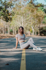 A woman is sitting on the side of a road, wearing a grey top and grey pants. She is smiling and she is enjoying the outdoors