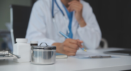A professional and focused Asian female doctor in scrubs is working and reading medical research on her laptop in her office at a hospital.