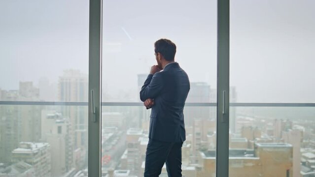 Thoughtful businessman looking cityscape at office panoramic window back view