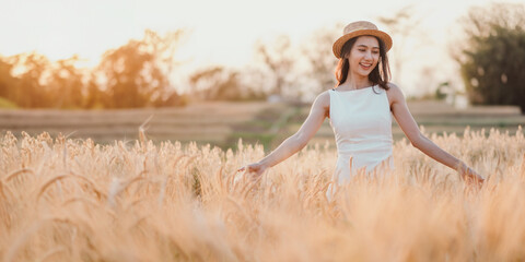 A woman is standing in a field of tall golden wheat. She is wearing a white dress and a straw hat....