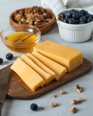 Sliced cheese on a wooden board with honey and blueberries