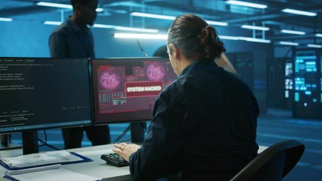 Multiethnic programmer team in server farm workspace surprised by data threatened by hacking attack on computers. Diverse colleagues scrambling to protect data center from unauthorized access