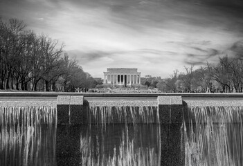 A monochrome photograph of the Lincoln Memorial in Washington D.C., viewed from across a reflective...