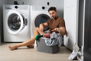 Happy man sorting clothes near washing machine in laundry room. man sits on the floor of a house...