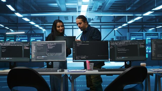 Multiracial colleagues in server hub workspace collaborating to fix servers providing computing resources for workloads. Engineers doing brainstorming while supervising data center supercomputers