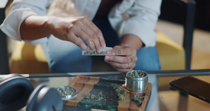 Marijuana, person and rolling paper with hands in home for smoking with high or relax with pleasure. Cannabis, joint and pot with headphones on weekend for 420 with natural cbd or weed addiction