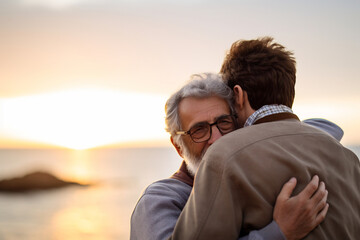Elderly man and adult son embracing on a beach at sunset, sharing an emotional and heartfelt moment, with the ocean in the background