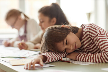 Selective focus shot of tired kid sitting at desk in classroom relaxing with eyes closed during...