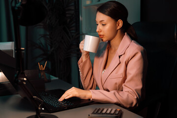 Beautiful sitting businesswoman with pink suit drinking coffee while searching business project...