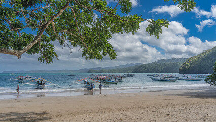 Many Filipino bangka boats are anchored and moored to the shore of the turquoise ocean. The waves...