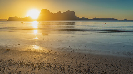 A calm romantic sunset on a tropical island. The setting sun is shining from behind the mountains....
