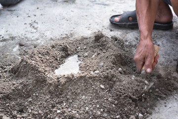 An adult man's hands are mixing a mixture of sand, cement and water as a basic building material