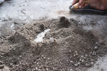An adult man's hands are mixing a mixture of sand, cement and water as a basic building material