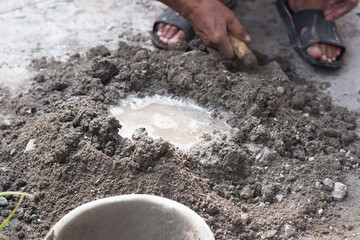 An adult man's hands are mixing a mixture of sand, cement and water as a basic building material