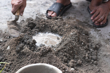 An adult man's hands are mixing a mixture of sand, cement and water as a basic building material