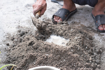 An adult man's hands are mixing a mixture of sand, cement and water as a basic building material