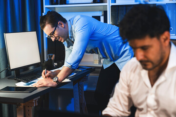 Colleagues concentrating on their job task at night home office behind desk while another man with...