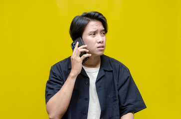 an overthinker young Asian man in pensive mood holding phone with sad and thoughtful expression. Asian man holding phone while questioning and wondering.