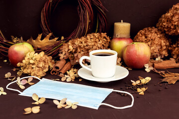 Cup of coffee, removed medical mask, blue surgical protective mask in autumn composition