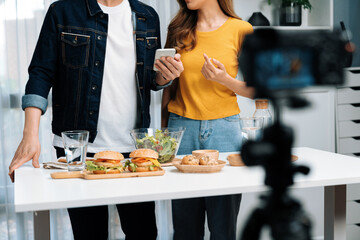 Cropped view of chef influencers reading comment on phone for answering time on social media cooking show channel live streaming with salad, bun bread and hamburger record by camera video. Infobahn.