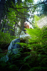 Adult mature woman 40-60 in a green long fairy dress in forest. Photo shoot in style of dryad and queen of nature. Fairy who loves nature in beautiful green summer forest. Concept of caring for nature