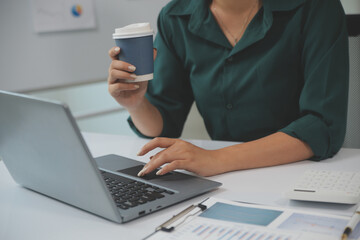 Beautiful young smiling Asian businesswoman working on laptop and drinking coffee, Asia businesswoman working document finance and calculator in her office.