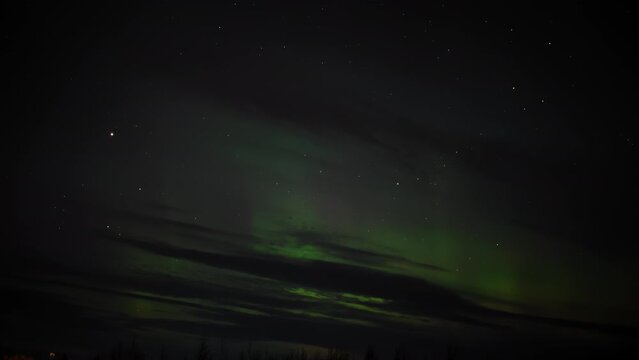 Night sky adorned with faint green Northern Lights, scattered stars, and dark clouds creating a mysterious and serene celestial scene