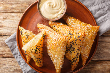 Triangular sesame puff pastry filled with chicken, cheese and herbs close-up in a plate on a wooden table. Horizontal top view from above