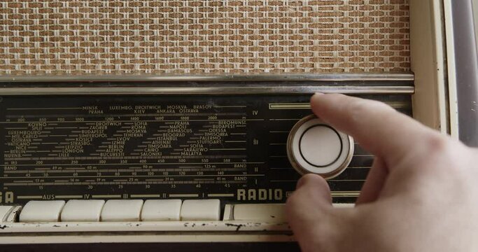 A man adjusts the tuning dial on an old-fashioned radio, focusing on finding a specific frequency station.