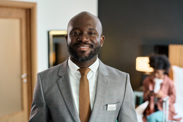 Front view portrait of bearded adult Black man wearing suit as hotel manager smiling at camera...