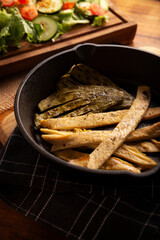 Roasted chicken breast cut into strips, roasted in a cast iron skillet accompanied by roasted nopales and fresh salad, served on a rustic wooden table. Simple and nutritious homemade recipe.