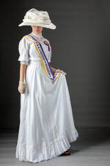 American Victorian or Edwardian Suffragette with historically accurate purple and gold sash and and rosette against a plain studio backdrop