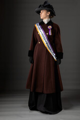 American Victorian or Edwardian Suffragette with historically accurate purple and gold sash and and rosette against a plain studio backdrop